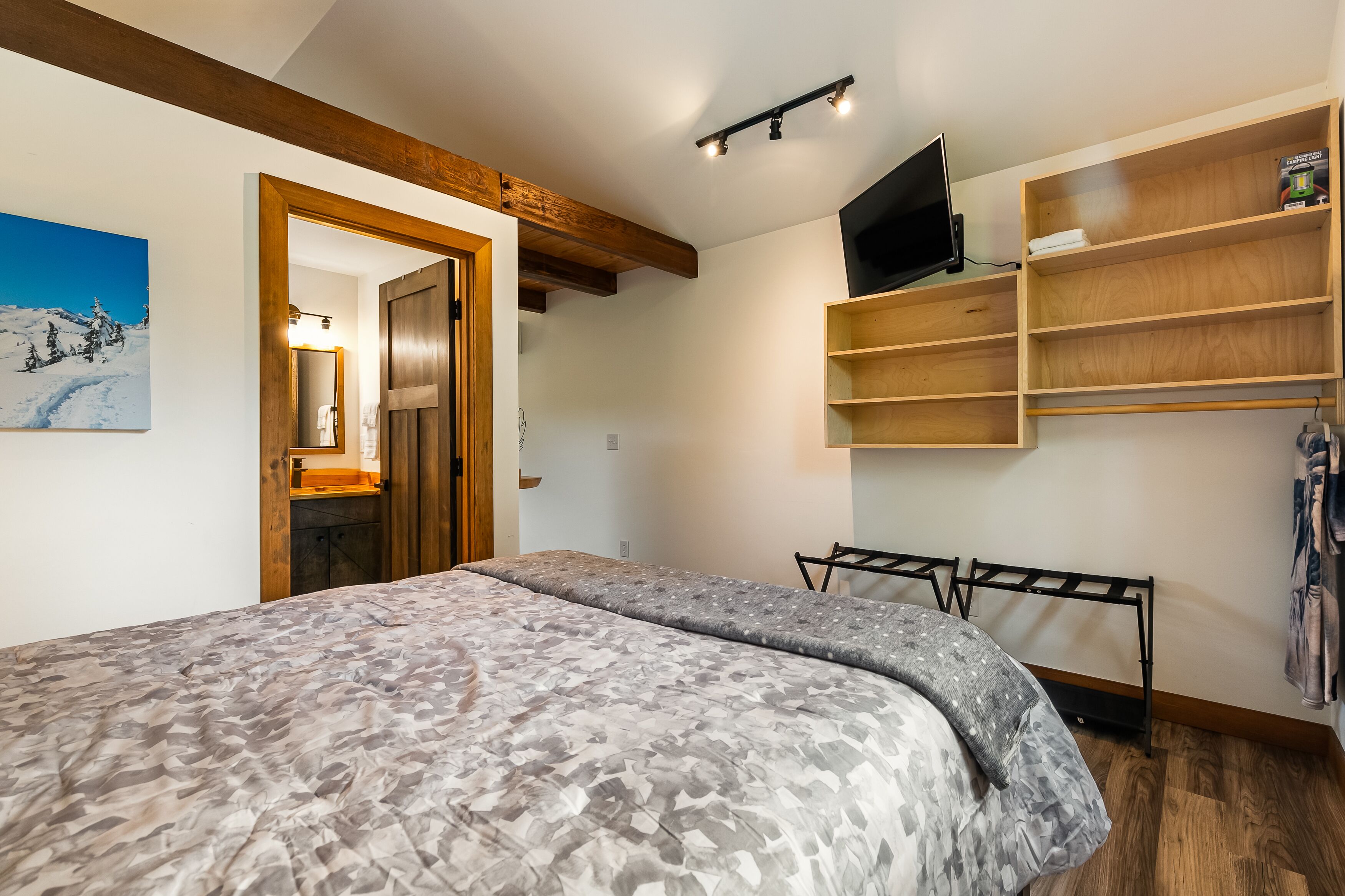 A bedroom with a bed, a wooden shelf unit, a TV, and a painting on the wall.