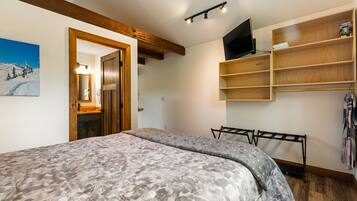 A bedroom with a bed, a wooden shelf unit, a TV, and a painting on the wall.