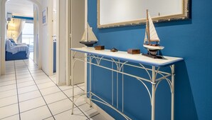 Un couloir avec un mur bleu, un sol carrelé de blanc, une console en métal blanc sur laquelle est posé un modèle de voilier, et un miroir au-dessus.