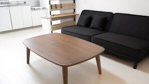 A modern living room with a wooden coffee table, a black sofa, and a wooden shelving unit against the wall. - KARCHIBE ISHIGAKI (Ishigaki)
