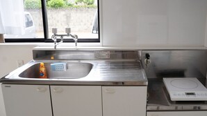 A kitchen with a stainless steel sink, a dish soap bottle, a weighing scale, and a window with a view of a parked car and greenery outside. - KARCHIBE ISHIGAKI (Ishigaki)