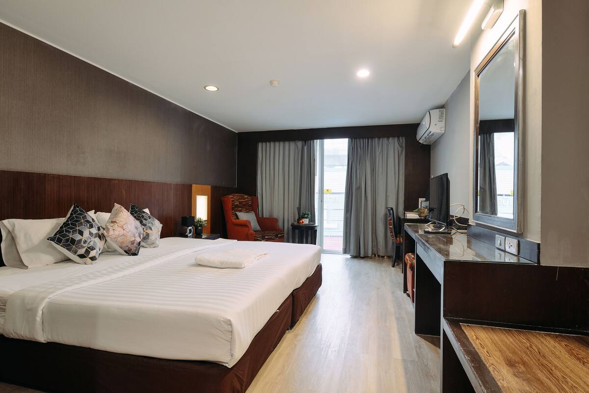 A hotel room with a large bed, a desk, a chair, a TV, and a window with curtains.