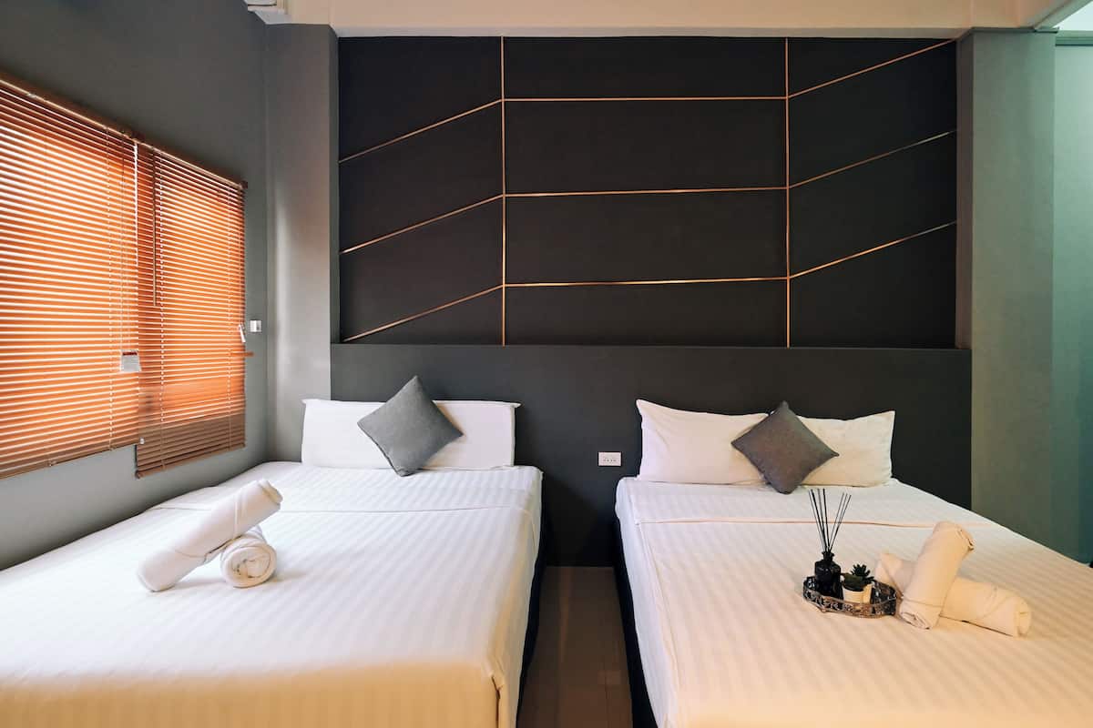 A hotel room with two beds, each with white linens and pillows, a modern headboard with geometric patterns, and a window with blinds.
