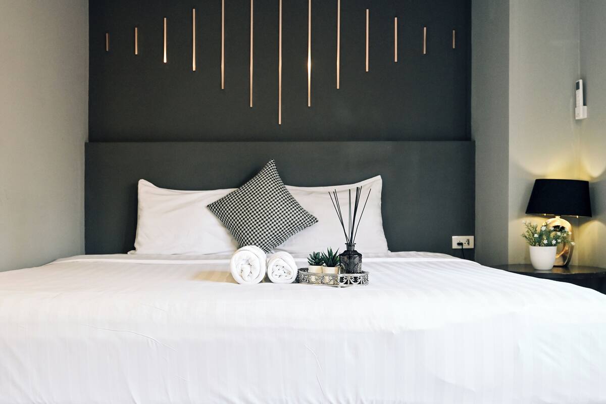 A neatly made bed with white linens, a black and white patterned pillow, and a small decorative tray with a plant and a candle.