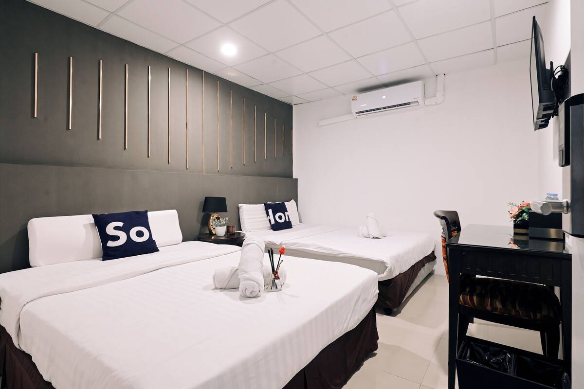 A hotel room with two beds, a desk, a chair, an air conditioner, and a TV.