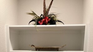 En hvid hylde med sammenrullet håndklæder i hvid og marineblå, et dekorativt bakke og en plante med røde blomster.