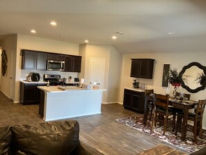 A modern kitchen with dark cabinets, a central island, and a dining area with a wooden table and chairs. - Entire house in Summit trail (Katy)