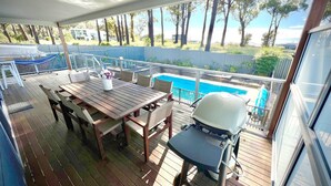Una terrazza esterna coperta con tavolo e sedie in legno, un barbecue e vista su una piscina.