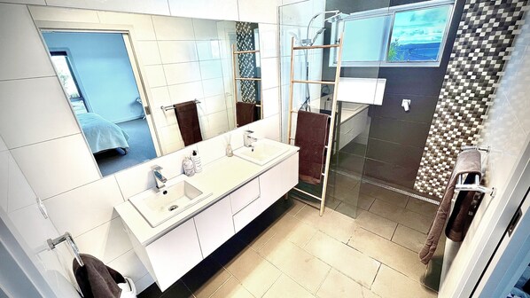 Un baño moderno con un espejo grande, un lavamanos blanco y una mampara de ducha de cristal.