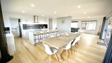 A modern kitchen with white cabinets, a central island with bar stools, and a dining area with a wooden table and white chairs.