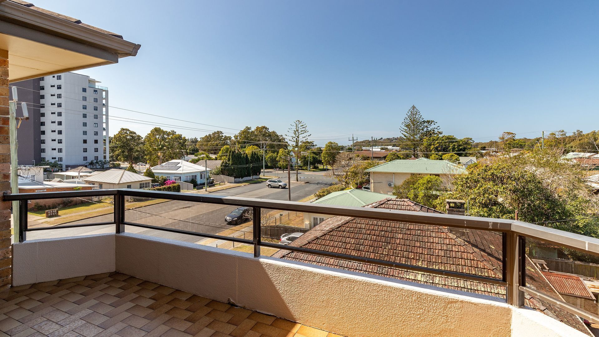A balcony with a view of a residential area, including a multi-story building and a street with cars.