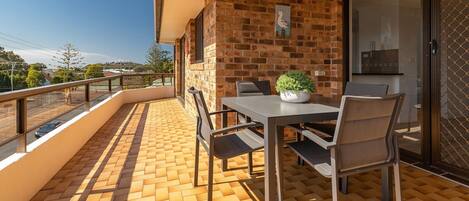 A balcony with a brick wall, a table with chairs, and a potted plant.