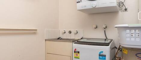 A laundry room with a washing machine, dryer, and a shelf with cleaning supplies.