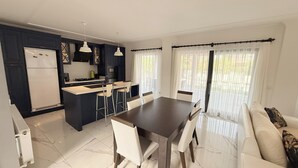 Een moderne keuken met een centraal eiland, witte barkrukken, een eettafel en een bank met kussens.