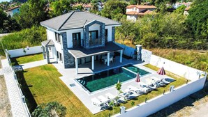 Een modern huis met twee verdiepingen, een zwembad, een overdekt terras en een goed onderhouden gazon.