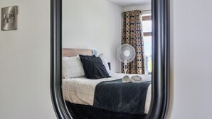 Ein Schlafzimmer mit einem Bett, einem Ventilator, einem Fenster mit Vorhängen und einem an der Wand befestigten Lichtschalter.
