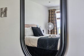 A bedroom with a bed, a fan, a window with curtains, and a wall-mounted light switch. - Modern Peaceful Open Plan 1-Bed Apartment Rutland (Rutland)