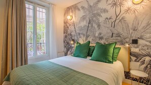 Ein Schlafzimmer mit einem großen Bett, grünen Kissen, einem Fenster mit Vorhängen und einer Wandmalerei von tropischen Pflanzen.