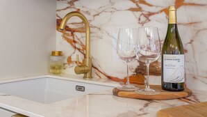 Eine Küche mit Marmor-Spritzschutz, einem goldenen Wasserhahn und einer Weinflasche auf der Arbeitsplatte.
