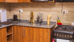 A kitchen with wooden cabinets, a gas stove, a microwave, and various utensils. - Beautiful 1-Bed apartment in the heart of Kampala (Kampala)