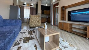 A living room with a blue sofa, a wooden coffee table, and a TV on a wooden stand. - Beautiful 1-Bed apartment in the heart of Kampala (Kampala)