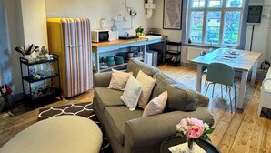 En moderne stue med sofa, spisebord og et køkkenområde med et stribet køleskab.