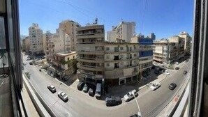 A view of a city street with multi-story buildings, cars parked along the side, and a clear blue sky. - 2 Bed Flat - Sleeps 6 - Pets - Parking - Wifi (Metn)
