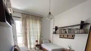 A bedroom with a bed, a bedside table, a small desk, a chair, a shelf with books, and a window with curtains. - 2 Bed Flat - Sleeps 6 - Pets - Parking - Wifi (Metn)
