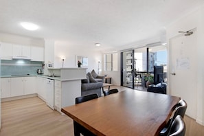 Et moderne køkken med hvide skabe, et træspisebord og en grå sofa.