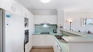 Een kleine keuken met witte kastjes, een inbouwoven, een spoelbak en een aanrecht.