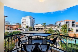 En balkon med et bord og stole, med udsigt over et boligområde med huse og en swimmingpool.
