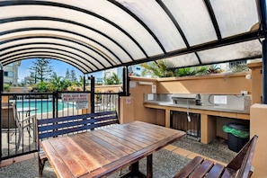 An outdoor pool area with a covered seating area, a grill, and a pool gate sign. - Paradise Ocean 2 Bedroom Apartment (Miami)