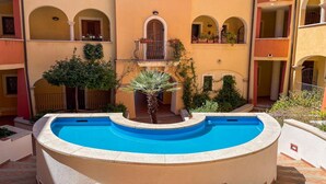 A courtyard with a central swimming pool, surrounded by balconies and potted plants. - La Porta Sul Mare in Golfo Aranci (Golfo Aranci)