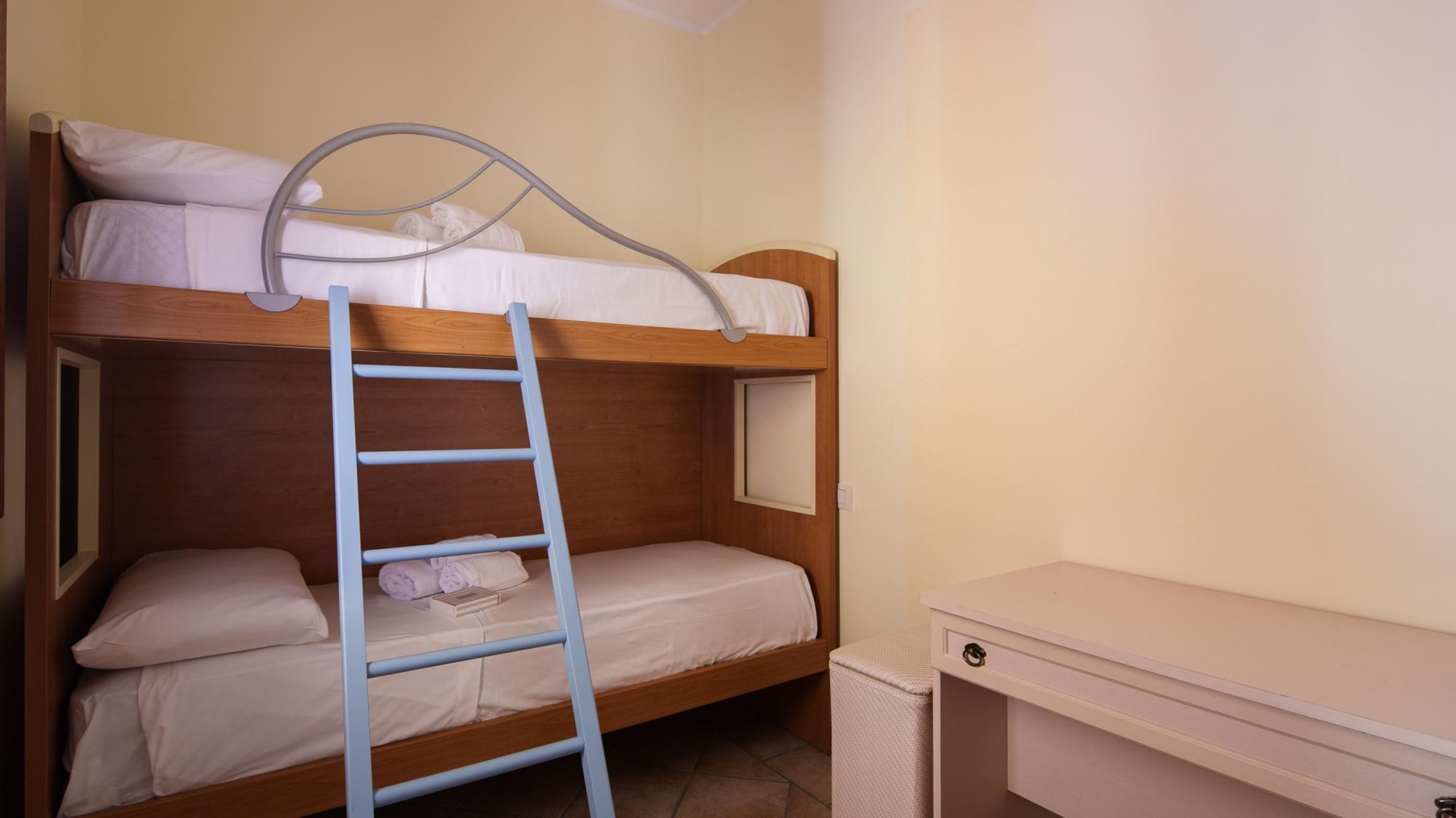 A bunk bed with a ladder, a bedside table, and a small desk.