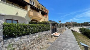 A coastal hotel with a wooden walkway, stone wall, and lush greenery. - La Porta Sul Mare in Golfo Aranci (Golfo Aranci)