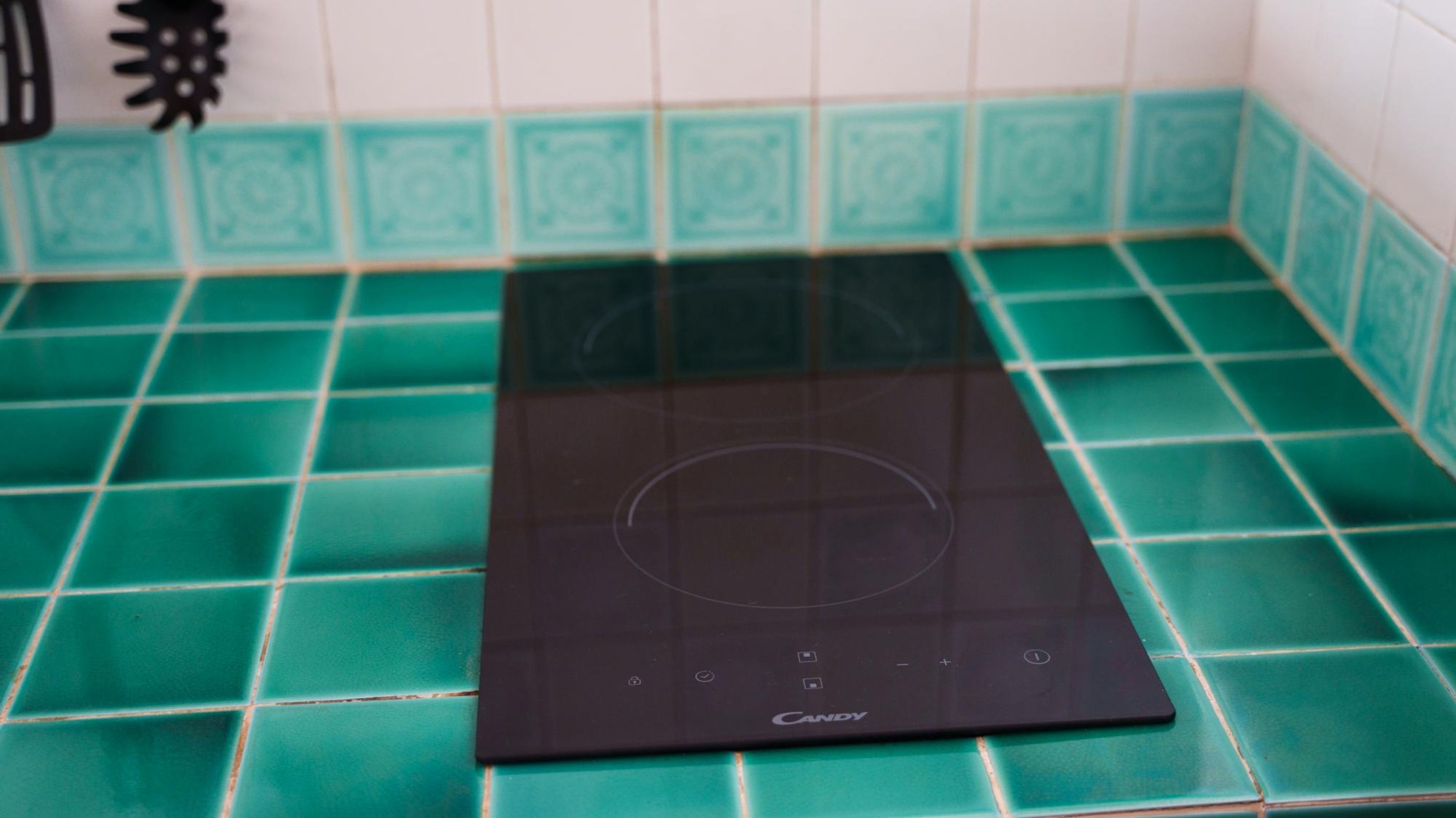 A black induction cooktop on a green-tiled kitchen countertop.
