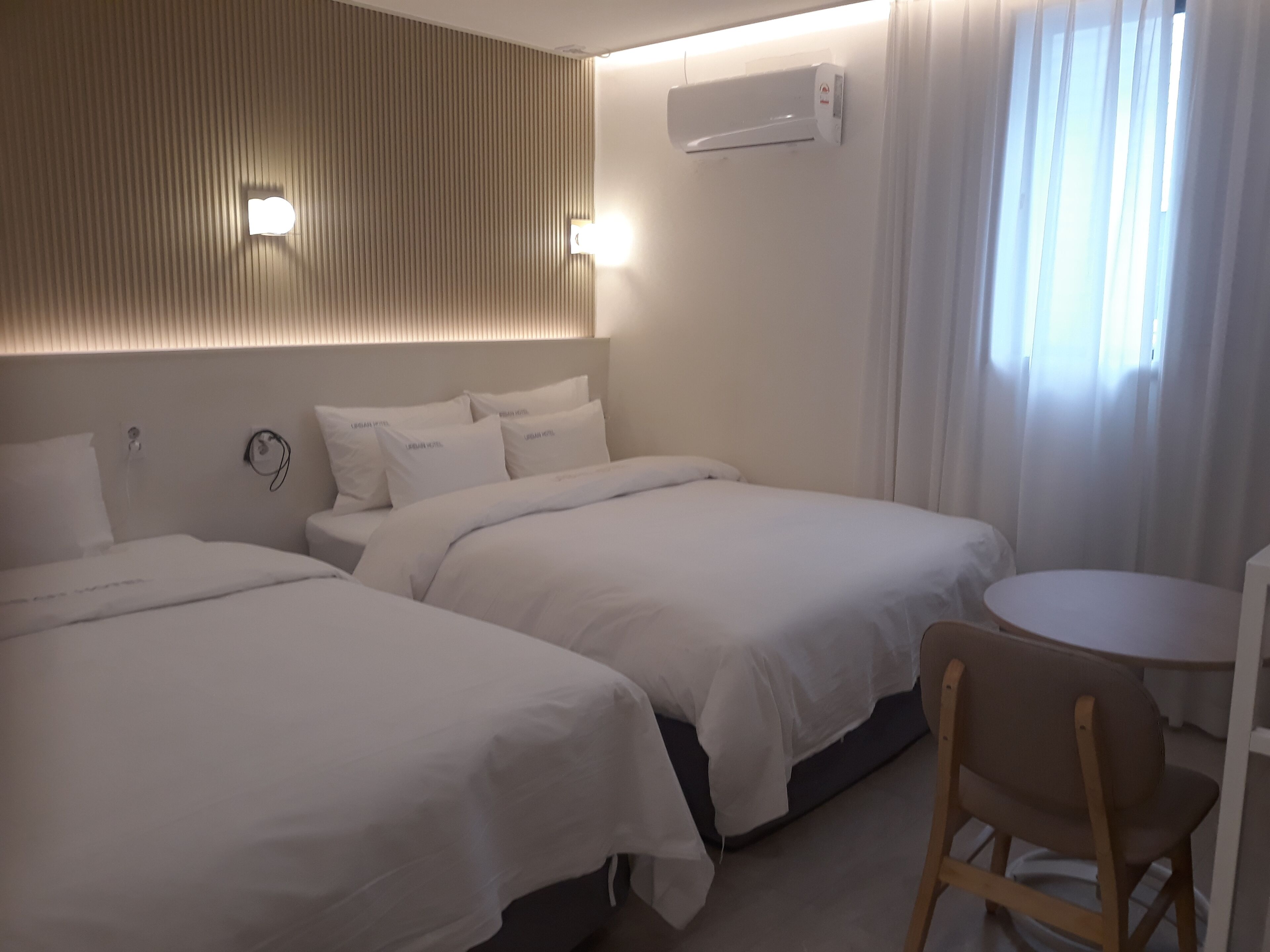 Une chambre d’hôtel avec deux lits, une petite table ronde, une chaise et un appareil de climatisation fixé au mur.