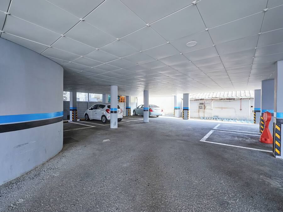 A parking garage with concrete pillars, white walls, and a tiled ceiling.