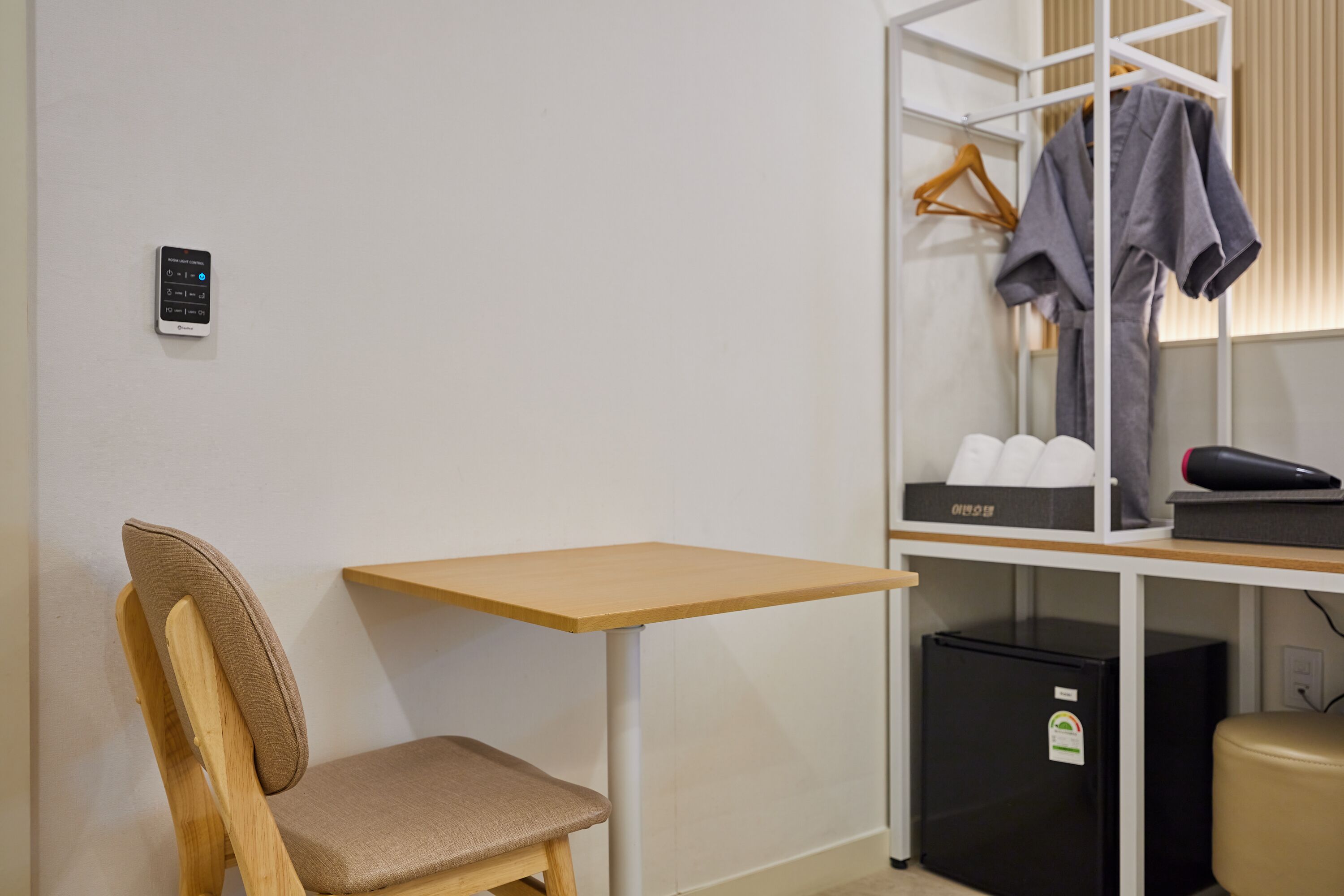 Habitación pequeña con una silla de madera, una mesita, un armario con ropa colgada y un electrodoméstico negro.