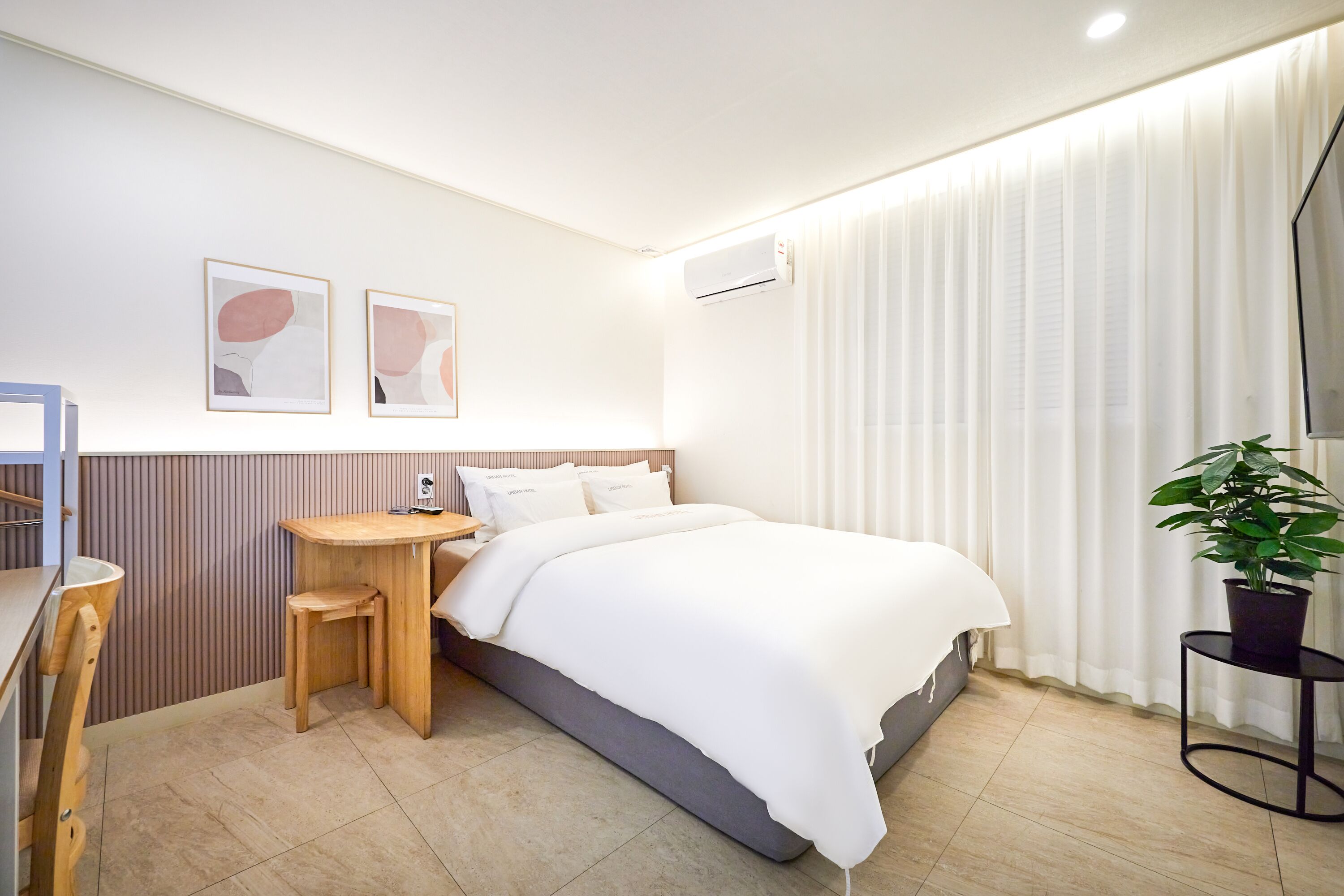 A modern hotel room with a bed, a desk, a chair, and a potted plant.