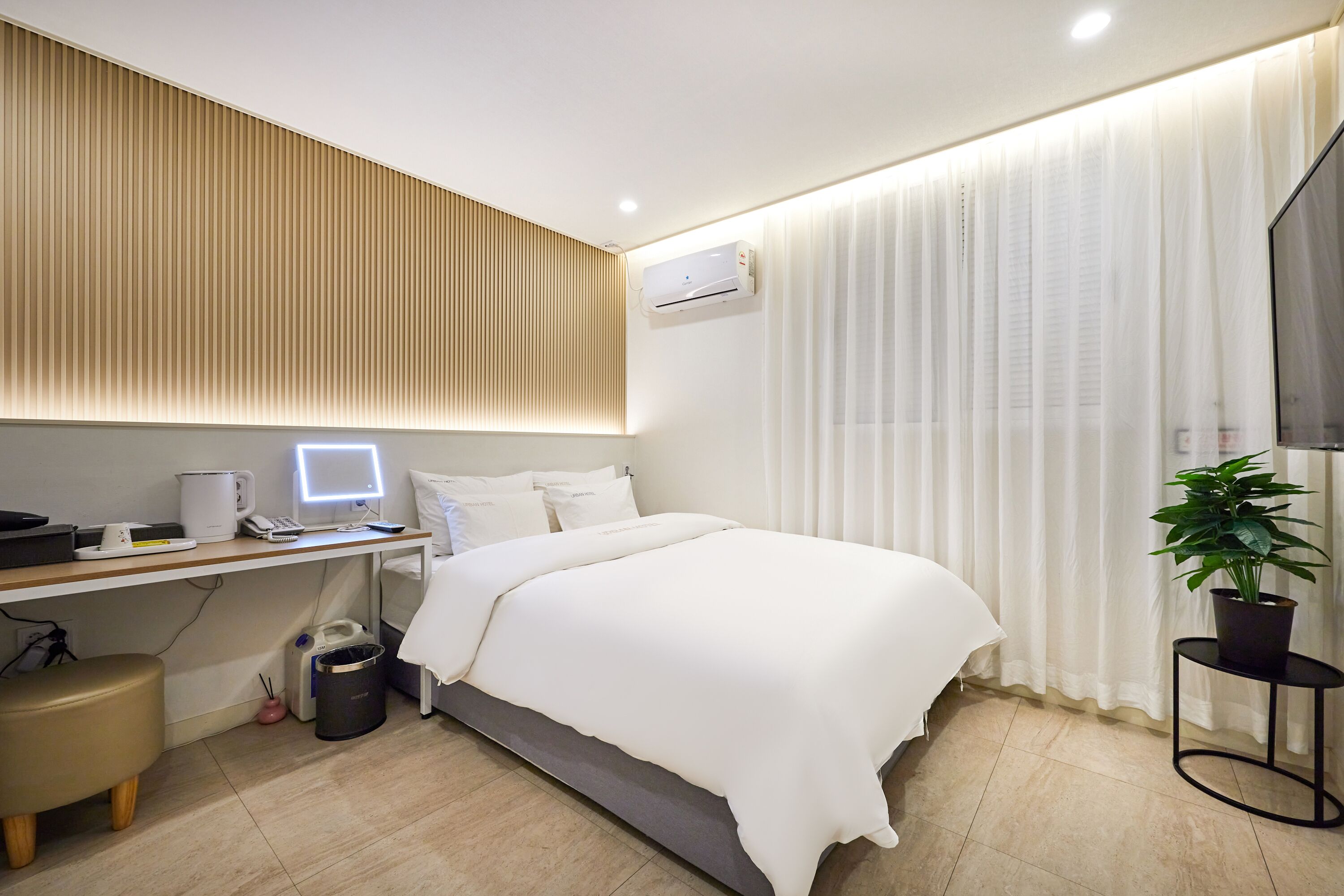 Ein modernes Hotelzimmer mit Bett, Schreibtisch und einer Topfpflanze.