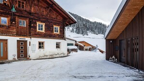 Una strada innevata in un villaggio con edifici in legno, una montagna sullo sfondo e un cielo sereno.