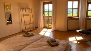 Een slaapkamer met een groot bed, een ladder, een stoel en uitzicht op het buitengebied door een raam.