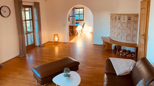 Een ruime woonkamer met houten vloer, een bank, een houten bankje, een kleine tafel en een kast.