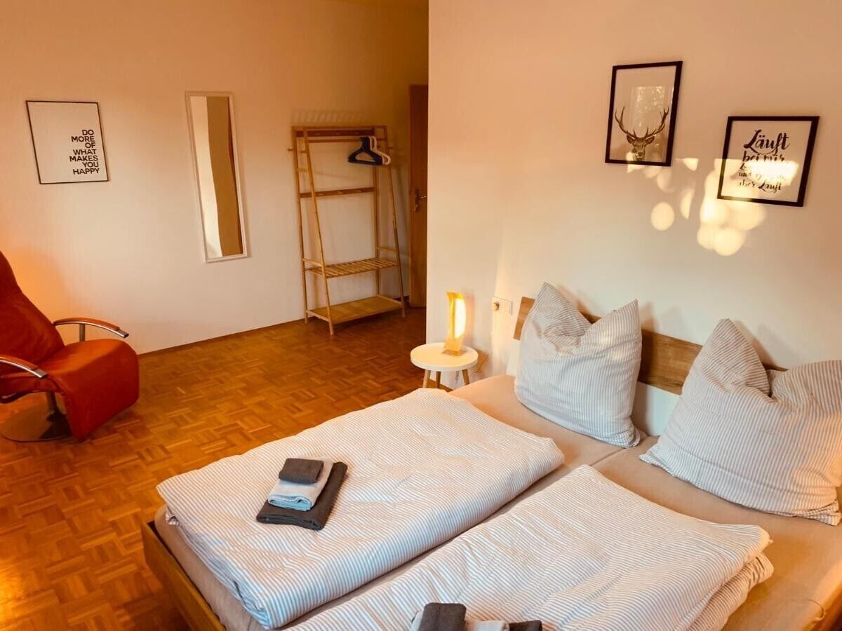 Ein Schlafzimmer mit zwei Betten, einem roten Sessel, Holzboden, einem Nachttisch mit Lampe und Wanddekorationen.