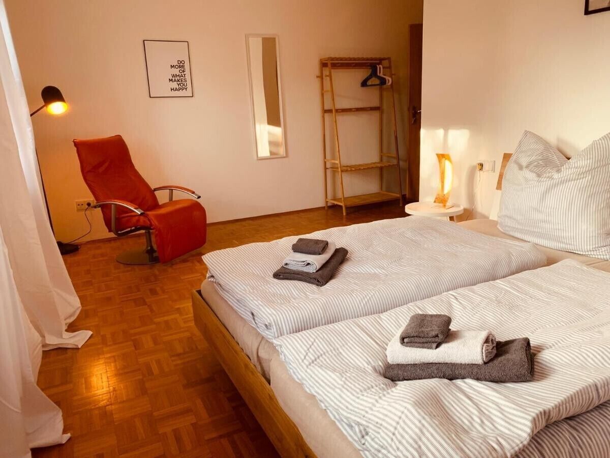 A hotel room with a bed, a red chair, a mirror, a shelf, and a wall with a motivational quote.