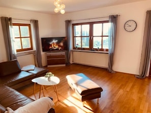 Un salon comprenant un canapé, un pouf, une petite table, un téléviseur et une cheminée.