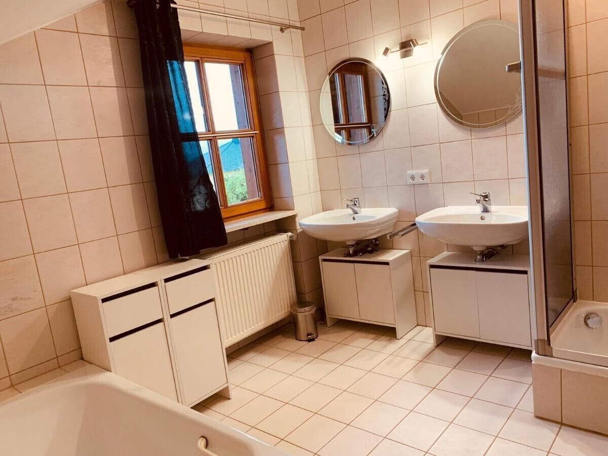 Et badeværelse med to vaske, et badekar, et vindue med gardin og et spejl.