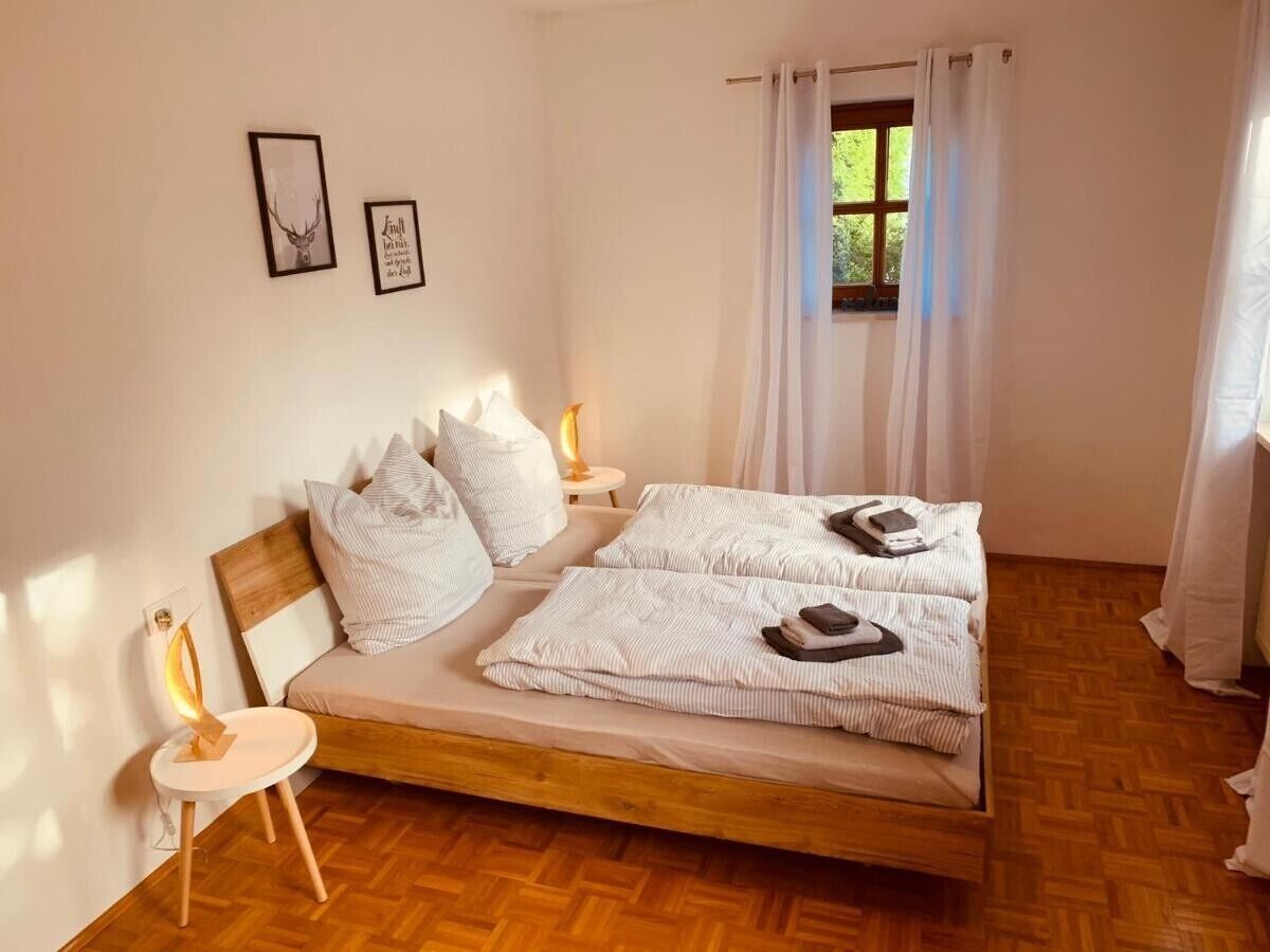 Ein Schlafzimmer mit einem hölzernen Bett, weißer Bettwäsche, einem Nachttisch mit Lampe und einem Fenster mit Vorhängen.