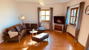 Een woonkamer met een zithoek, een salontafel, een televisie en een open haard.